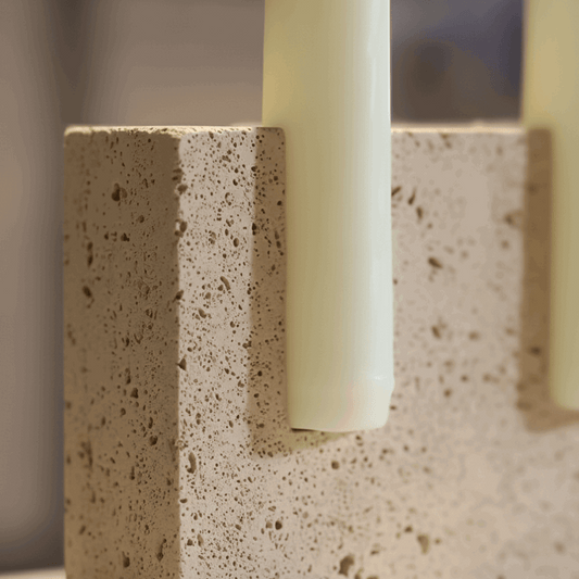 Detalhe do travertino com poros e variações naturais em castiçal artesanal, luz de vela acolhedora.