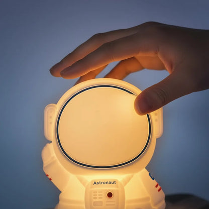 Mão tocando o sensor da luminária astronauta feita de silicone macio e seguro.