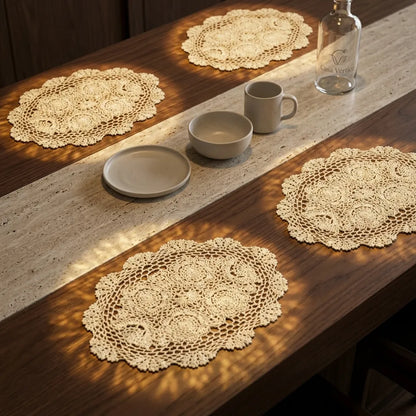 Conjunto de quatro jogos americanos de crochê handmade oval em algodão bege, com padrão floral, sobre mesa de nogueira e mármore Travertino.