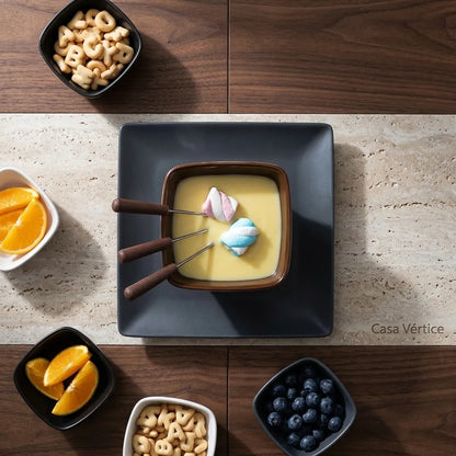 Vista superior de mesa posta com fondue de cerâmica, frutas e marshmallows sobre nogueira e travertino, padrão Casa Vértice.