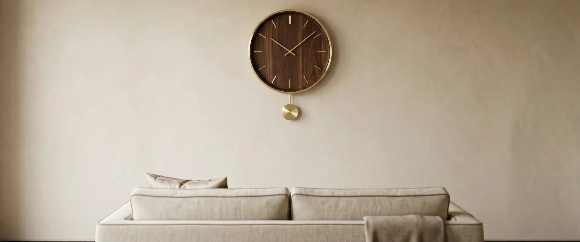 Banner de categoria CasaVértice Home Decor com foco em design de parede minimalista. Uma parede com textura de cimento queimado ou gesso em tom bege claro exibe, centralizado, um relógio de parede redondo e minimalista feito de madeira escura com aro metálico dourado e um pêndulo dourado suspenso. Abaixo do relógio, aparece o encosto de um sofá de linho contemporâneo em tom cru com uma manta de textura suave, destacando a elegância e a sobriedade do design de interiores atemporal.
